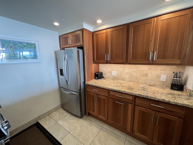 kitchen featuring light stone counters, light tile patterned floors, brown cabinets, stainless steel fridge with ice dispenser, and backsplash