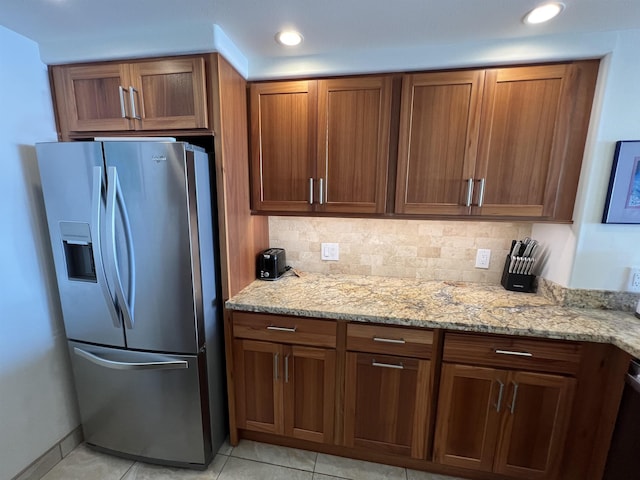 kitchen featuring light tile patterned floors, stainless steel refrigerator with ice dispenser, light stone countertops, and brown cabinets