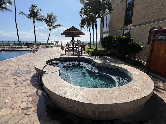 view of swimming pool with a patio, fence, a hot tub, and a water view