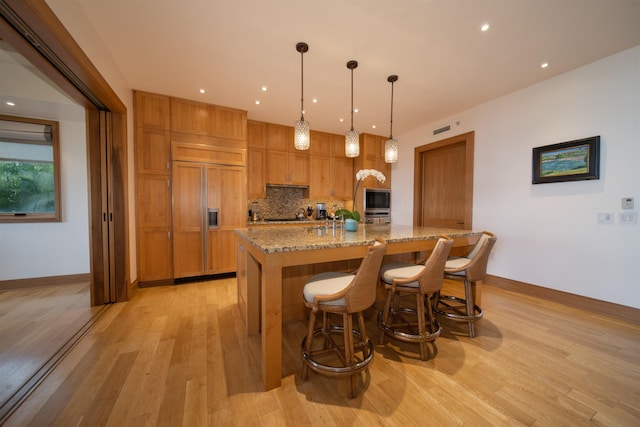 kitchen with decorative light fixtures, light hardwood / wood-style flooring, built in appliances, and light stone countertops