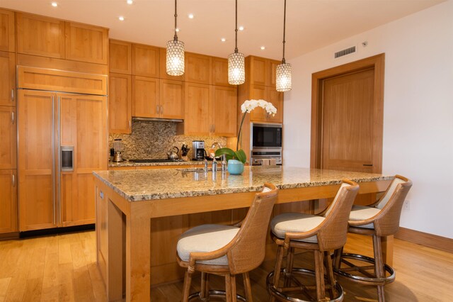 kitchen featuring pendant lighting, black appliances, tasteful backsplash, light stone counters, and a center island with sink