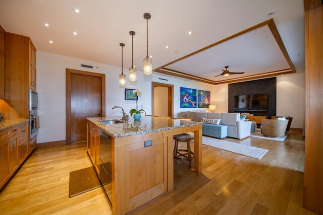 kitchen with light hardwood / wood-style floors, a kitchen breakfast bar, sink, pendant lighting, and an island with sink