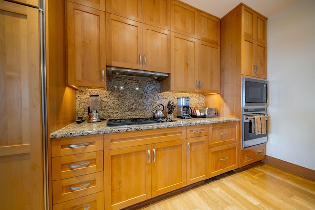 kitchen featuring light wood-type flooring, stainless steel appliances, light stone countertops, and tasteful backsplash