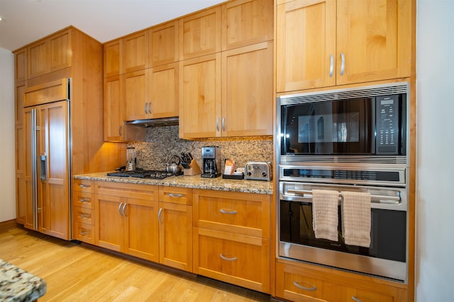 kitchen featuring black appliances, decorative backsplash, light stone countertops, and light hardwood / wood-style floors