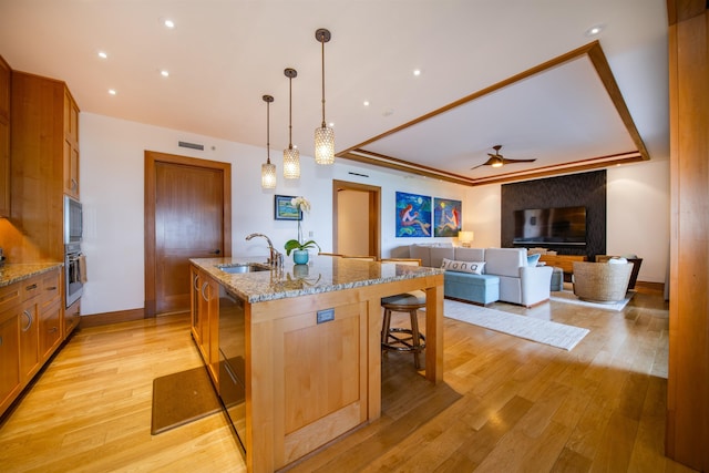 kitchen with sink, hanging light fixtures, a kitchen island with sink, and light stone counters