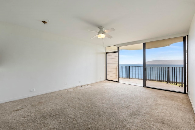 carpeted spare room featuring expansive windows, ceiling fan, and baseboards