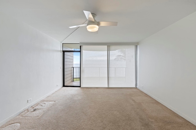 carpeted spare room with baseboards, a wall of windows, and a ceiling fan