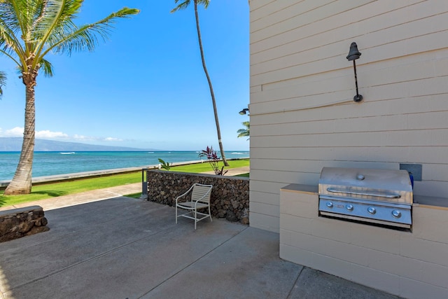 view of patio with area for grilling, a water view, a grill, and a view of the beach