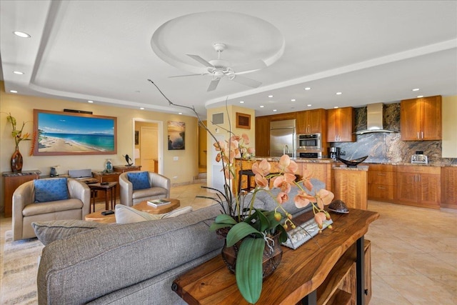 living room featuring a raised ceiling, ceiling fan, and light tile patterned floors