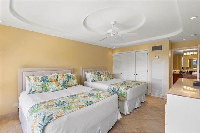 bedroom with ceiling fan, a raised ceiling, light tile patterned floors, and a closet