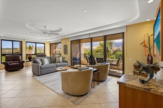 tiled living room with a raised ceiling, a wealth of natural light, and ceiling fan