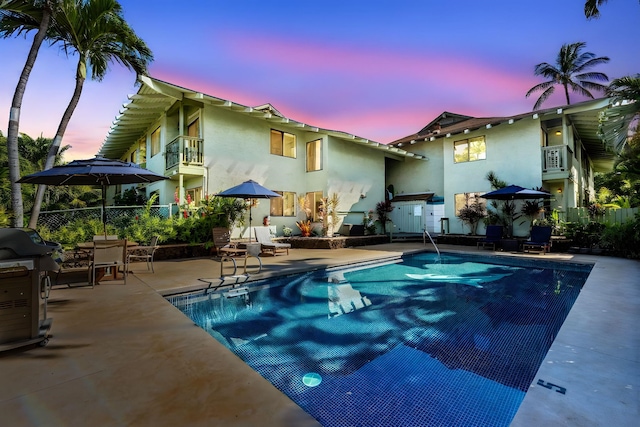 pool at dusk with grilling area and a patio area