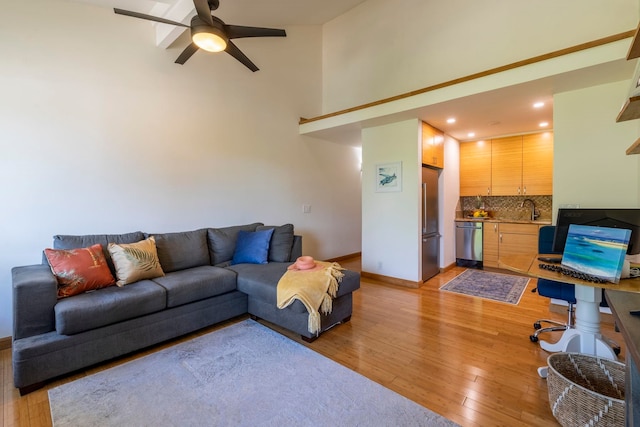 living room with ceiling fan, sink, light hardwood / wood-style floors, and a high ceiling