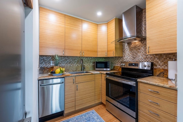 kitchen with sink, appliances with stainless steel finishes, decorative backsplash, wall chimney exhaust hood, and light wood-type flooring