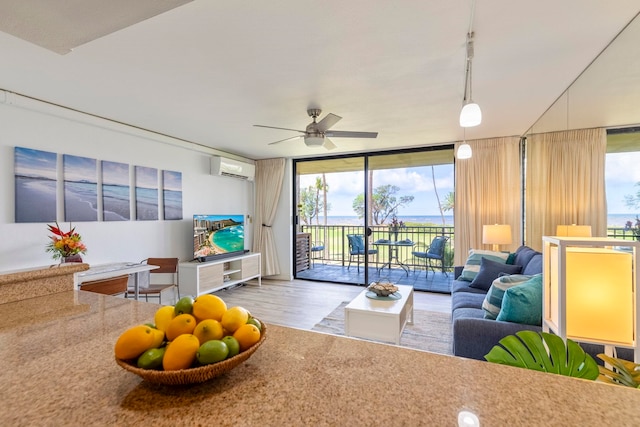 living room featuring a ceiling fan, a wall unit AC, wood finished floors, and floor to ceiling windows