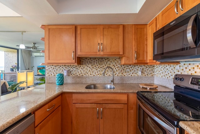 kitchen featuring a sink, backsplash, a ceiling fan, light stone countertops, and appliances with stainless steel finishes