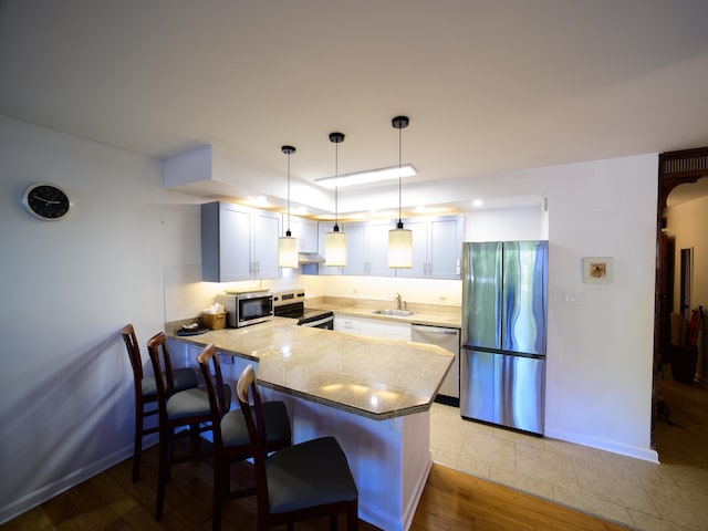 kitchen with white cabinetry, sink, stainless steel appliances, kitchen peninsula, and a kitchen bar