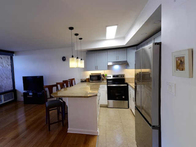 kitchen with a kitchen breakfast bar, light stone countertops, appliances with stainless steel finishes, decorative light fixtures, and kitchen peninsula