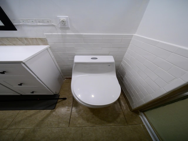 bathroom with toilet, tile patterned floors, and tile walls