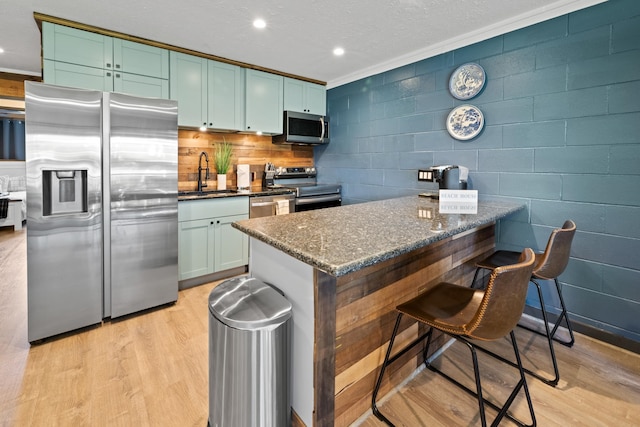 kitchen with appliances with stainless steel finishes, dark stone counters, a breakfast bar area, light hardwood / wood-style floors, and sink