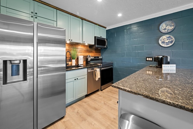 kitchen with sink, dark stone counters, crown molding, light hardwood / wood-style floors, and stainless steel appliances