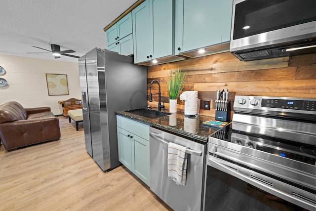 kitchen featuring appliances with stainless steel finishes, dark stone counters, ceiling fan, light hardwood / wood-style floors, and sink