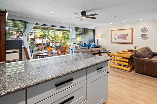 kitchen featuring ceiling fan, a textured ceiling, dark stone countertops, and light hardwood / wood-style floors