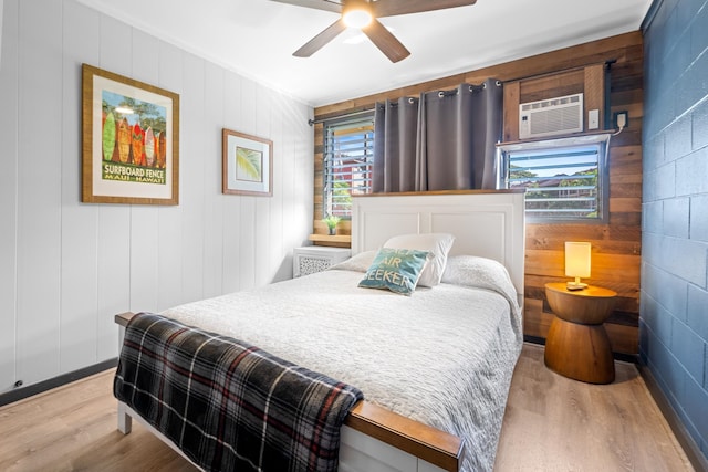 bedroom with multiple windows, light hardwood / wood-style floors, ceiling fan, and a wall mounted air conditioner