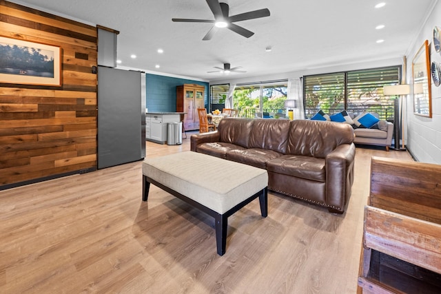 living room featuring wooden walls, ceiling fan, ornamental molding, and light hardwood / wood-style floors