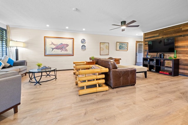 living room with ceiling fan, wooden walls, light wood-type flooring, and a textured ceiling