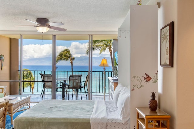 bedroom with a textured ceiling, a water view, expansive windows, and ceiling fan