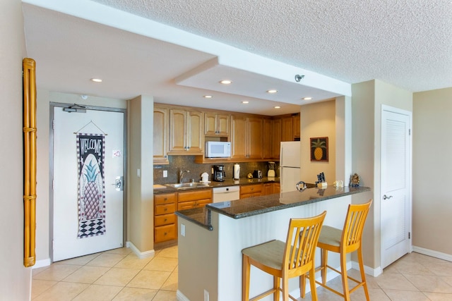 kitchen featuring kitchen peninsula, white appliances, sink, a breakfast bar area, and light tile patterned flooring