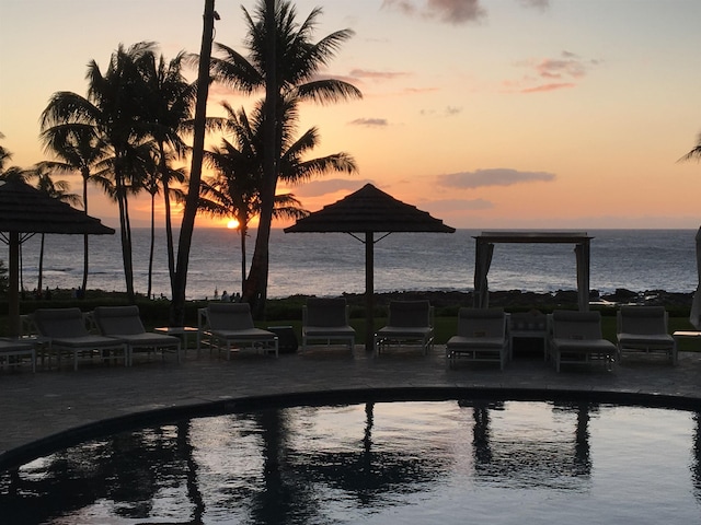 pool at dusk with a water view and a patio area