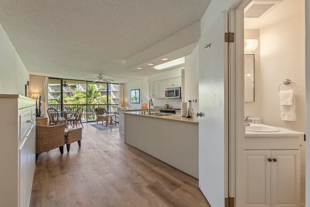 kitchen with stainless steel microwave, wood finished floors, a textured ceiling, floor to ceiling windows, and a sink