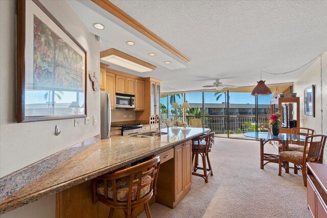 kitchen with appliances with stainless steel finishes, a kitchen bar, a sink, a textured ceiling, and light carpet