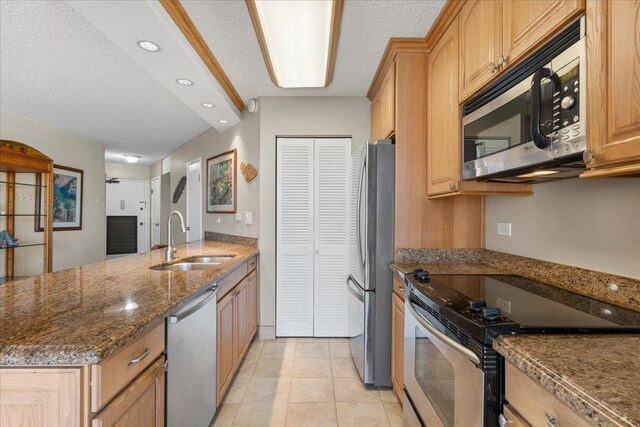 kitchen featuring appliances with stainless steel finishes, a sink, dark stone countertops, a peninsula, and a textured ceiling