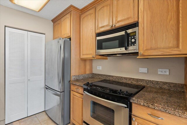 kitchen with stainless steel appliances, dark stone countertops, and light tile patterned floors