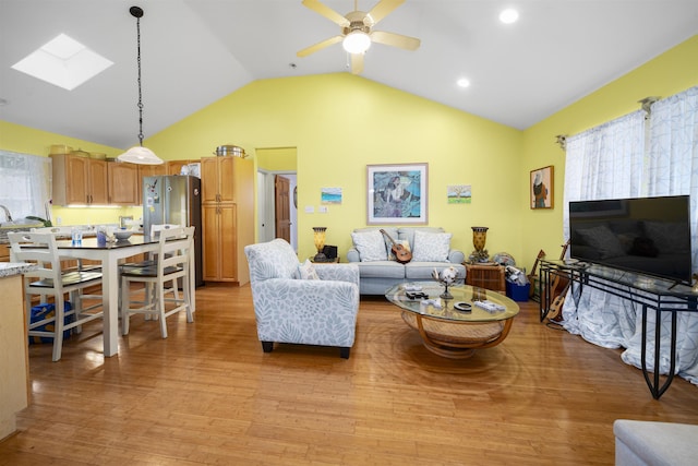 living room featuring lofted ceiling with skylight, light hardwood / wood-style floors, and ceiling fan