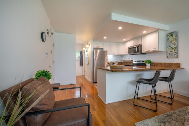 kitchen with appliances with stainless steel finishes, kitchen peninsula, white cabinets, dark stone counters, and light wood-type flooring