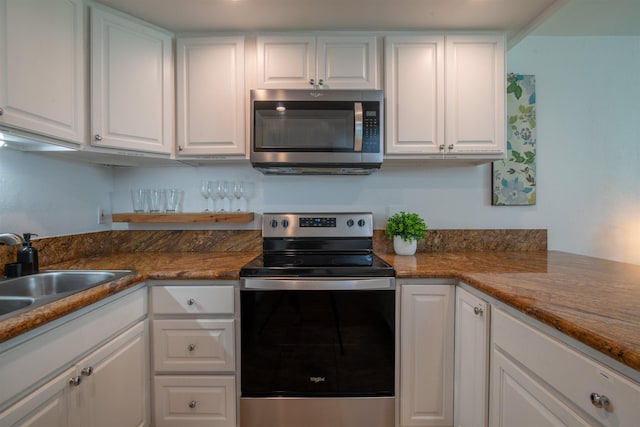 kitchen with appliances with stainless steel finishes, sink, dark stone counters, and white cabinets