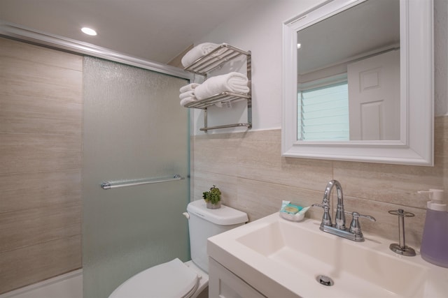 bathroom with vanity, a shower with shower door, tile walls, and toilet