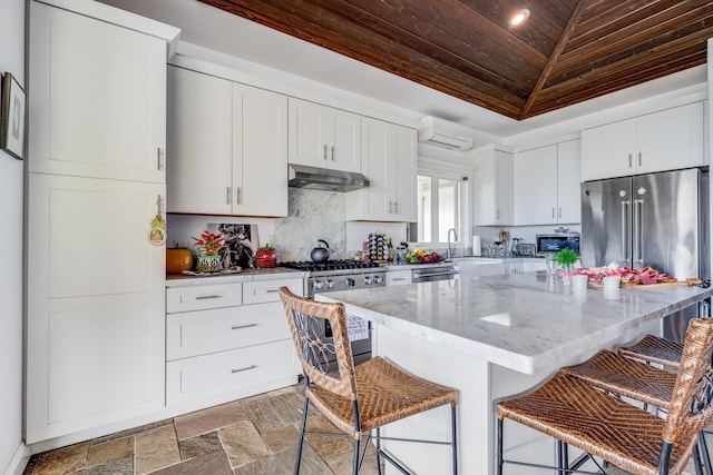 kitchen with a kitchen breakfast bar, appliances with stainless steel finishes, white cabinets, light stone counters, and wood ceiling