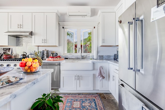 kitchen with a wall mounted AC, sink, white cabinets, stainless steel appliances, and wall chimney exhaust hood