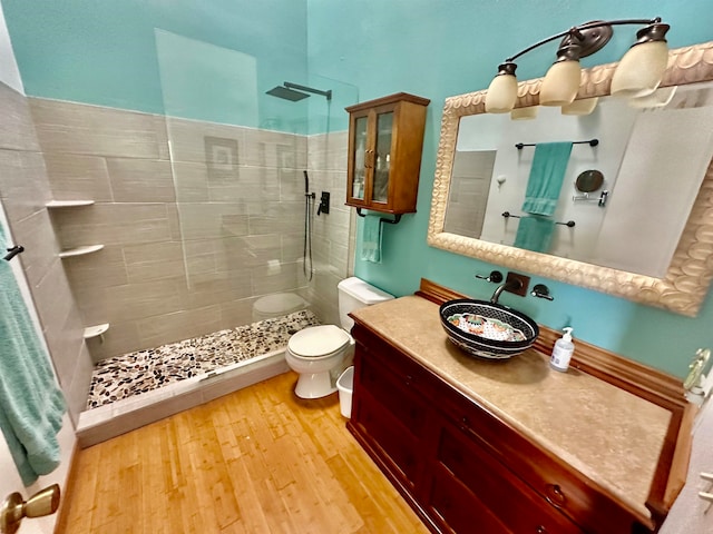 bathroom with hardwood / wood-style flooring, vanity, tiled shower, and toilet