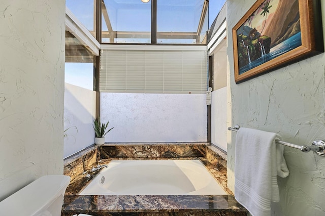 bathroom featuring a relaxing tiled tub and toilet