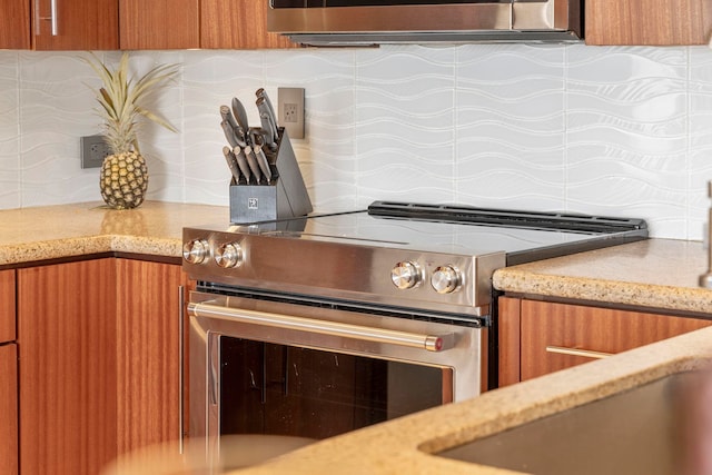 kitchen featuring backsplash, light stone counters, and stainless steel electric range