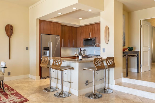 kitchen with light tile patterned floors, appliances with stainless steel finishes, a kitchen breakfast bar, decorative backsplash, and kitchen peninsula