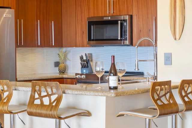 kitchen with tasteful backsplash, light stone counters, fridge, and a kitchen bar