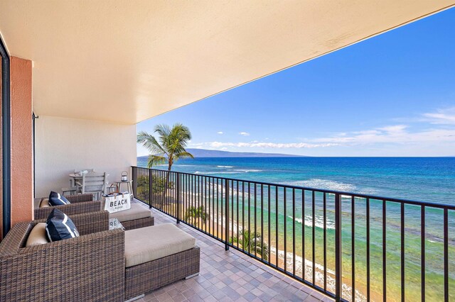 balcony with an outdoor living space, a water view, and a beach view