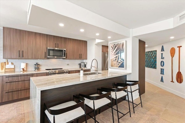 kitchen featuring stainless steel appliances, tasteful backsplash, light stone countertops, a breakfast bar, and sink